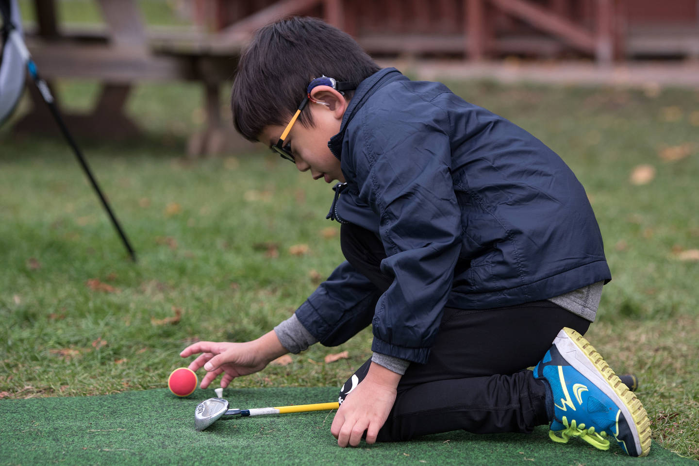 Young boy with hearing impairment putting golf ball on tee.