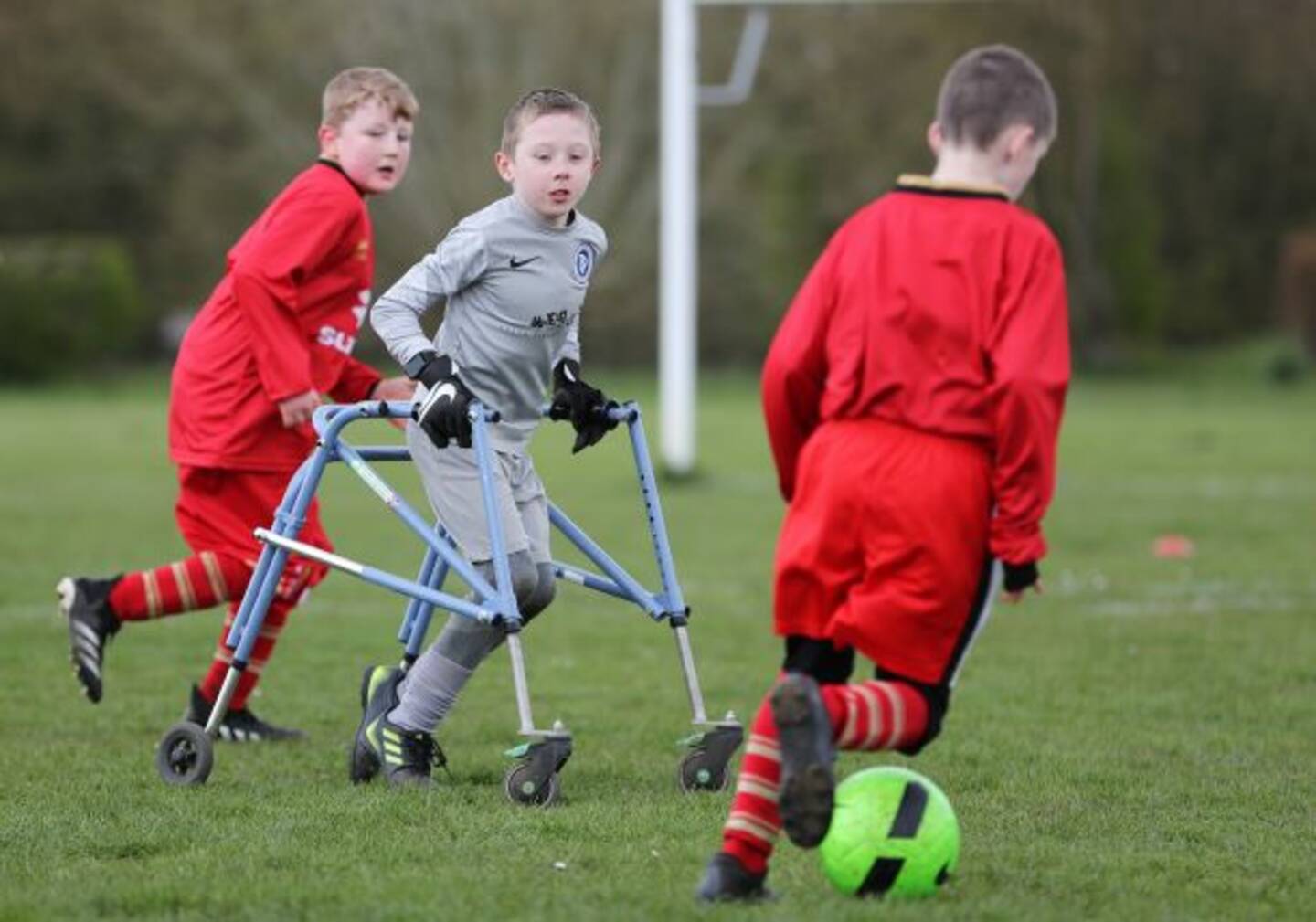 Three boys playing in a football match, one player is using a frame walker.