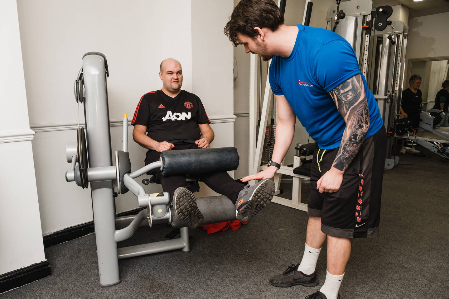Fitness instructor supporting man to use a leg cable weight machine in the gym