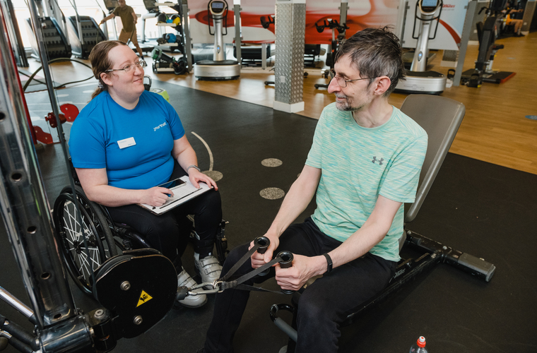 Catherine, a disabled personal trainer supporting client in the gym
