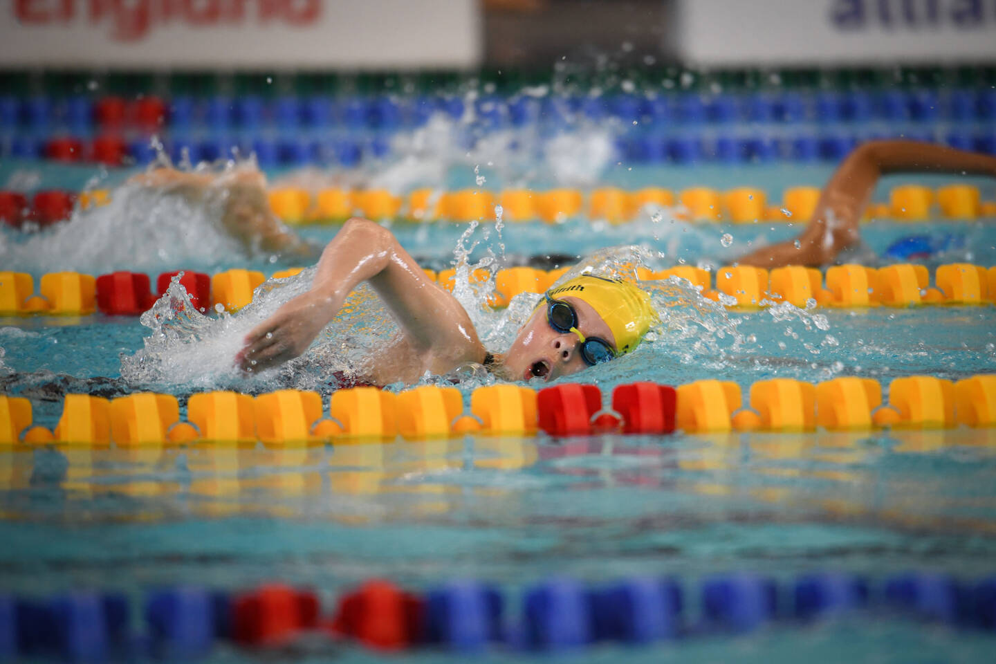 A swimmer in a yellow cap does front crawl down a swimming lane.
