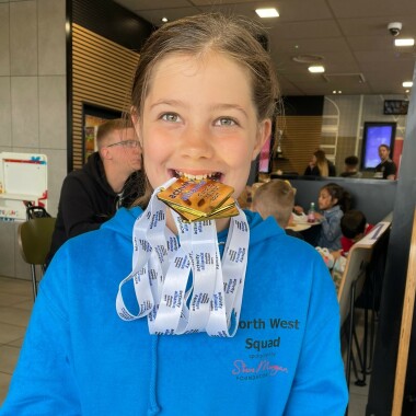 Freya Mason holds Activity Alliance medals between her teeth. 