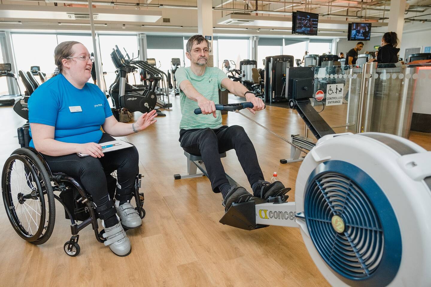 Disabled fitness instructor supporting her client to use the rowing machine in the gym