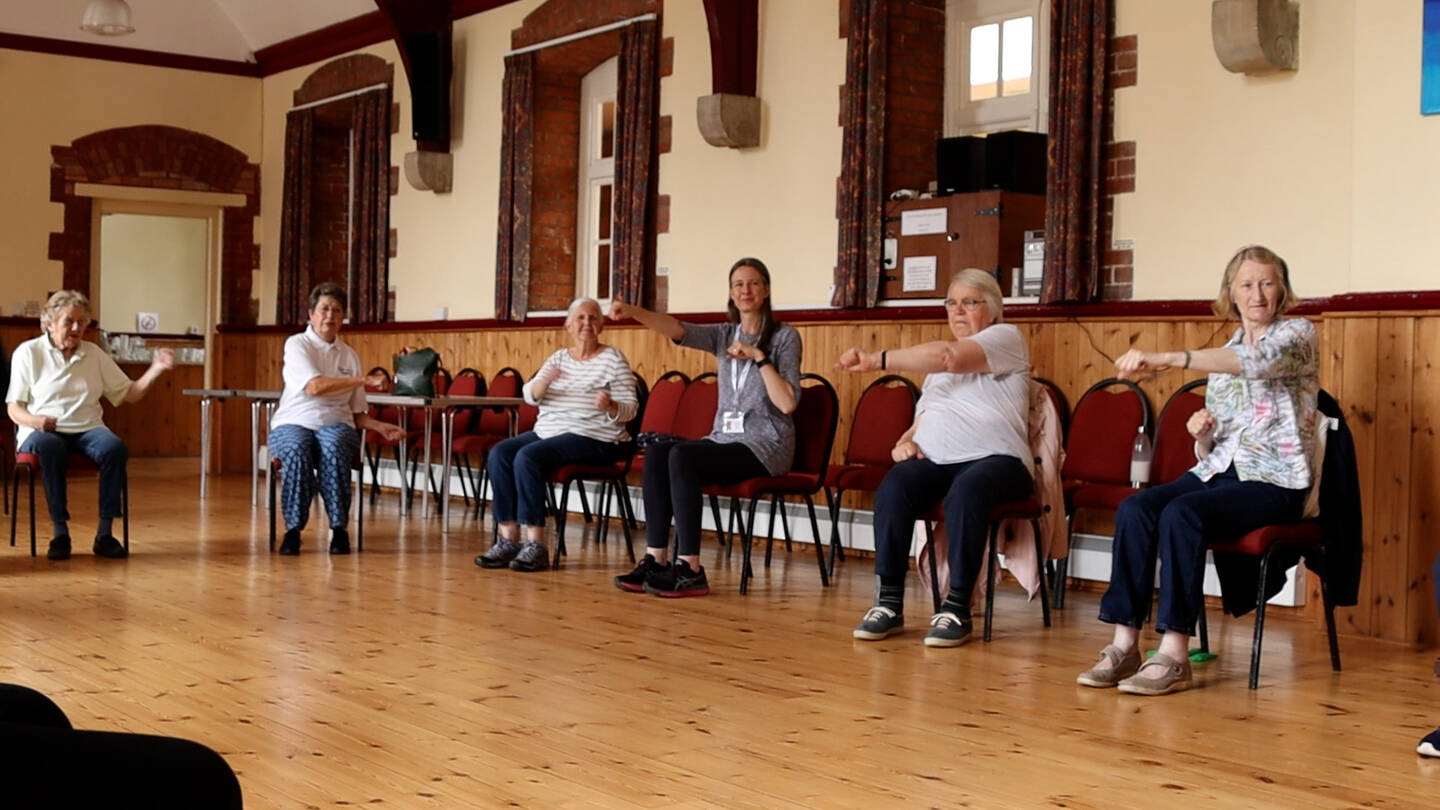 Group of older people taking part in seated exercise class. 